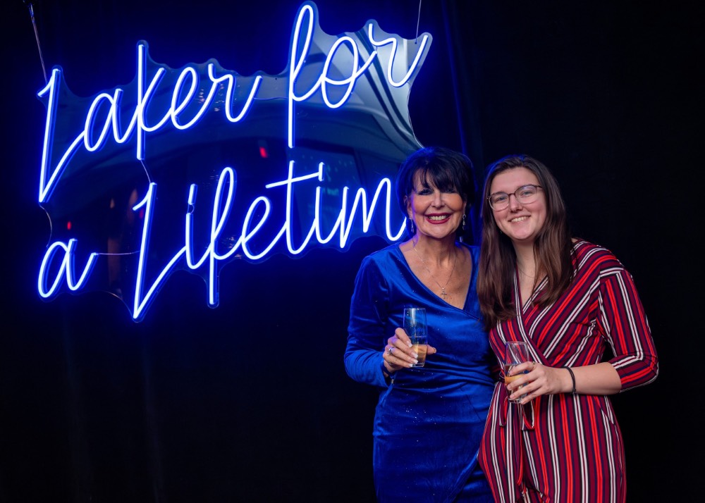 Girl in red dress and President Mantella stand in front of Laker for a Lifetime neon sign